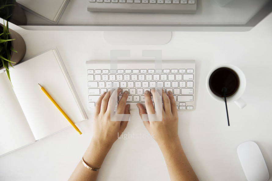 woman's hands typing on a desktop computer.