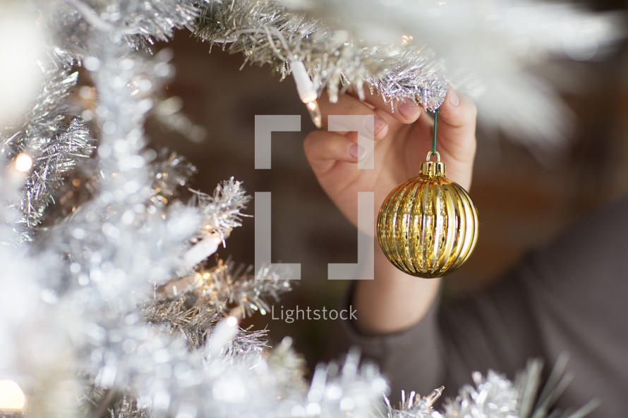 person hanging ornaments on a Christmas tree.