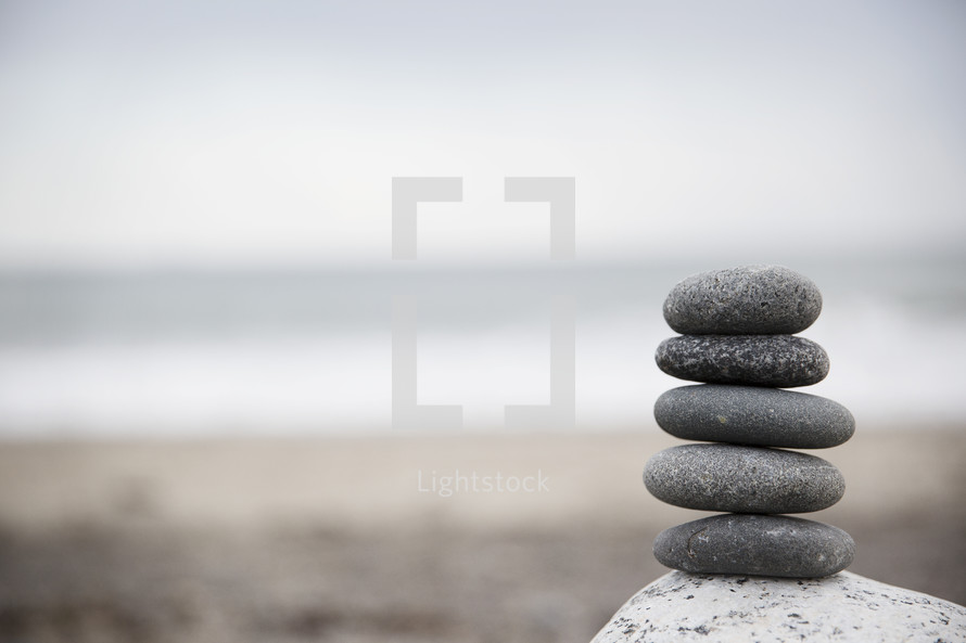 stacked stones on a rock with the ocean in the background