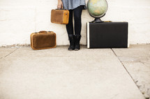 woman holding a suitcase and standing next to a globe 