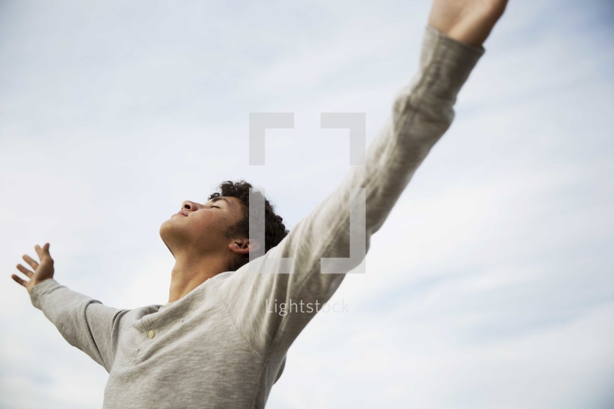teen boy with his hands raised in praise 