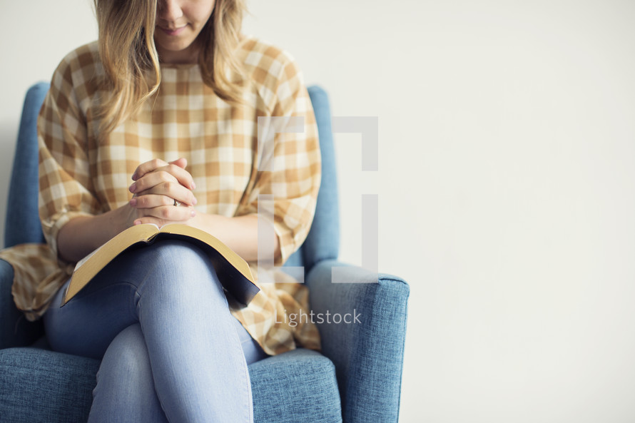 a woman sitting in a chair praying over an open Bible 