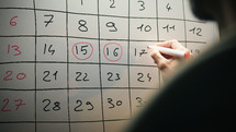 The man is circling the dates to remember on the calendar