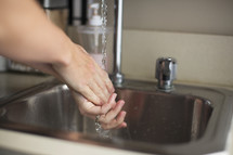 a  woman washing her hands in a sink.