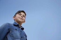 young boy standing under a blue sky