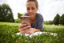a person sitting in the grass reading a Bible and checking her cellphone 