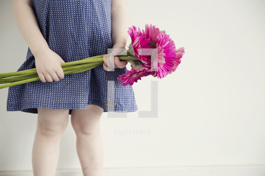 a little girl holding flowers at her waist. 