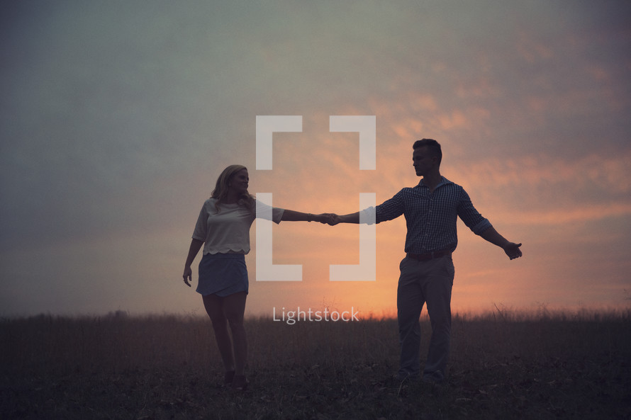 A man and a woman hold hands in a field at dusk.