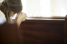 a woman with her head bowed in prayer over a pew 