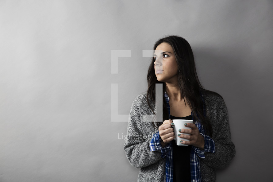 woman holding a coffee mug and looking away in thought. 