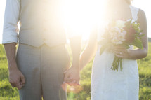 torsos of bride and groom holding hands 