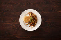 A white plate of a hamburger and french fries on a wooden table.
