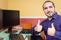 man with thumbs up sitting at a computer desk 