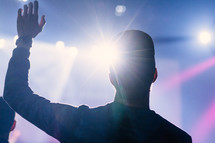 silhouette of a man with hand raised at a concert 