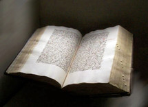 An old bible written in the original Hebrew or Greek manuscript language sitting in a museum with the book open for all to see and read to those who could read the language and understand it. 