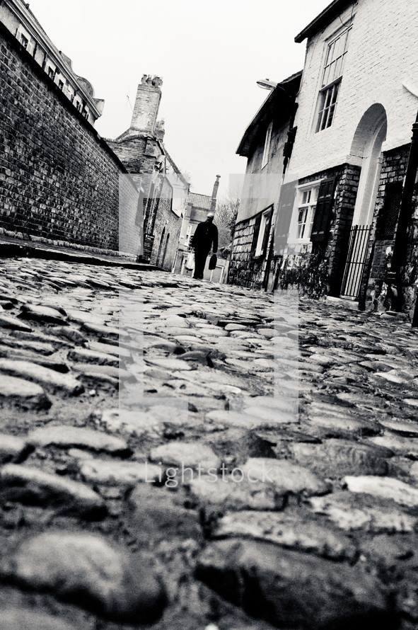 man walking down a cobblestone street 