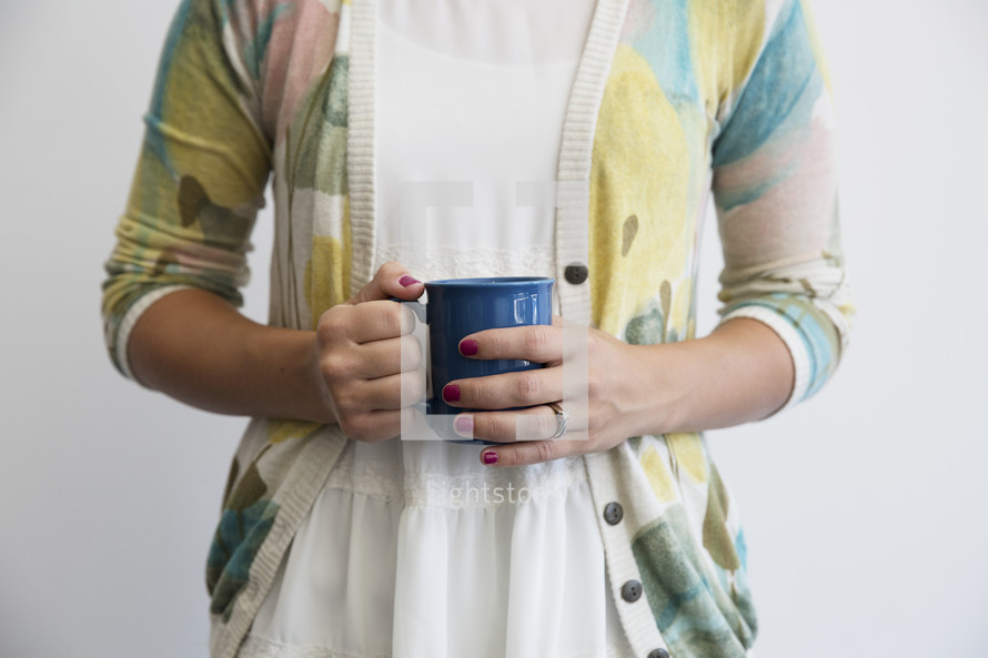 A woman in a sweater holding a blue coffee cup.