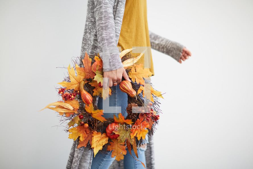a woman holding a fall wreath 