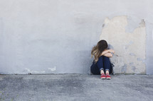 a sad woman crying sitting on a sidewalk 