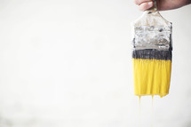 A paint brush dripping with yellow paint.