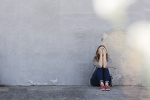 a woman hiding her face sitting on a sidewalk 