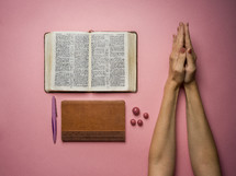 praying hands and open Bible on a pink background 