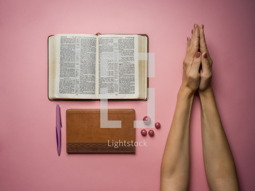 praying hands and open Bible on a pink background 