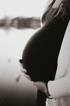 a pregnant silhouette against a sun setting on the lake 