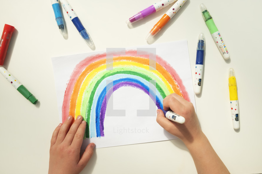 Personal perspective view of a caucasian boy colouring a rainbow