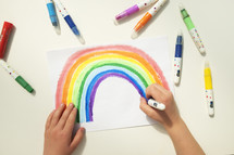 Personal perspective view of a caucasian boy colouring a rainbow