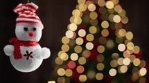 Tiny snowman decoration with Christmas tree in the background 