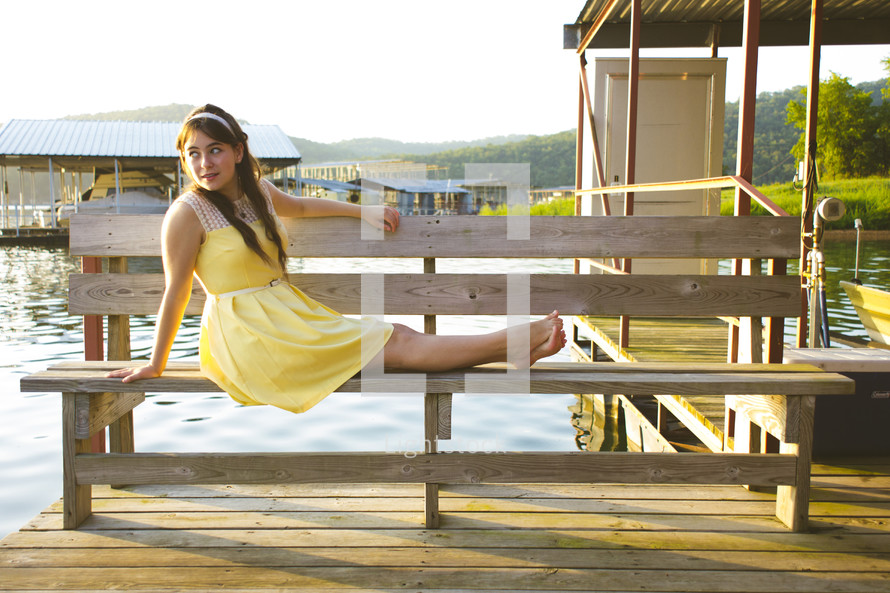teen girl in a yellow sundress sitting on a bench 