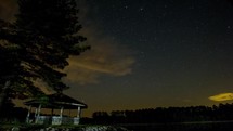 Timelapse of Night Sky and Clouds over Lake with Gazebo. 