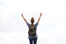 a woman with a backpack with hands raised giving peace signs 