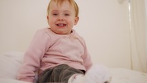 Cute baby girl sitting on a bed, playing, rolling and laughing
