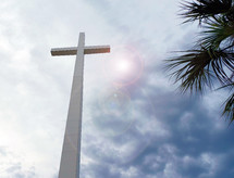 The Reach of the Cross - a large cross reaches from Heaven to Earth with clouds and palm trees waving in the wind to the right of the cross. 