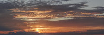 A panoramic view of the sun setting in the ocean with golden clouds fills the sky over Gotland, Sweden. 
