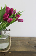 Purple tulips in a vase on a wooden table.