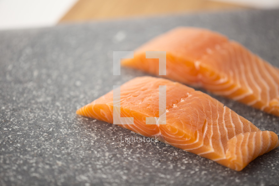 Two pieces of salmon on a cutting board.