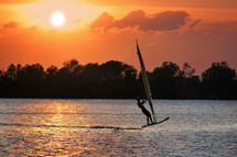Silhouette of a windsurfer on a lake at sunset.