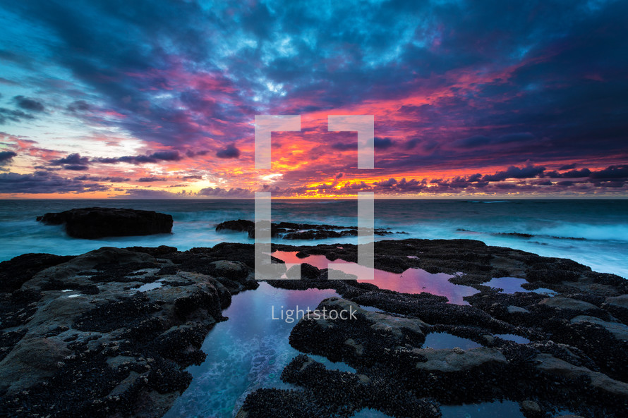 a purple and pink sky at sunset over tide pools 