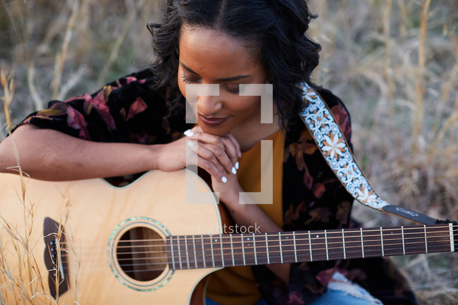 a woman sitting in a field with a guitar praying 