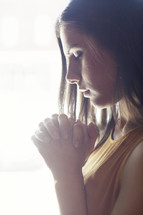 A young woman with hands clasped and head bowed in prayer.