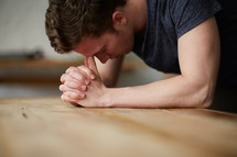a man with his head on praying hands on a table 