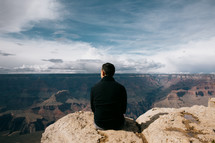 man sitting at the edge of a canyon landscape 