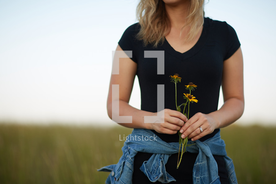 a young woman standing in a field of tall grass holding flowers 