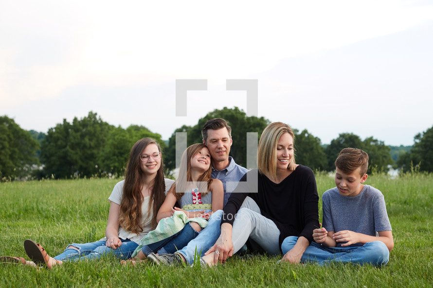a portrait of a family sitting together in grass