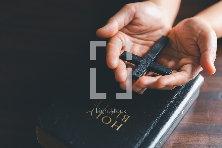 Wooden cross in open hands on a Bible