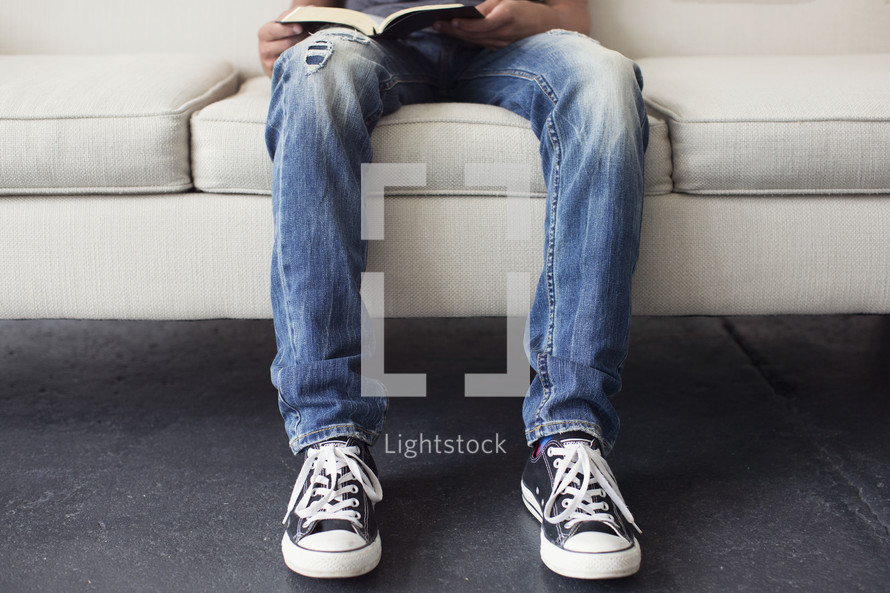 teen boy sitting on a couch reading a Bible 