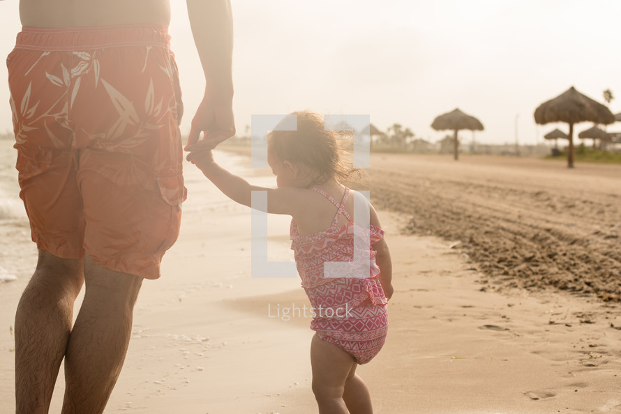 father and daughter holding hands on a beach 